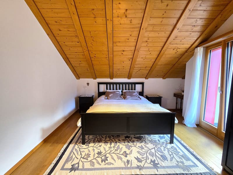 Bedroom with wooden ceiling, bed, nightstands, rug, and glass door.