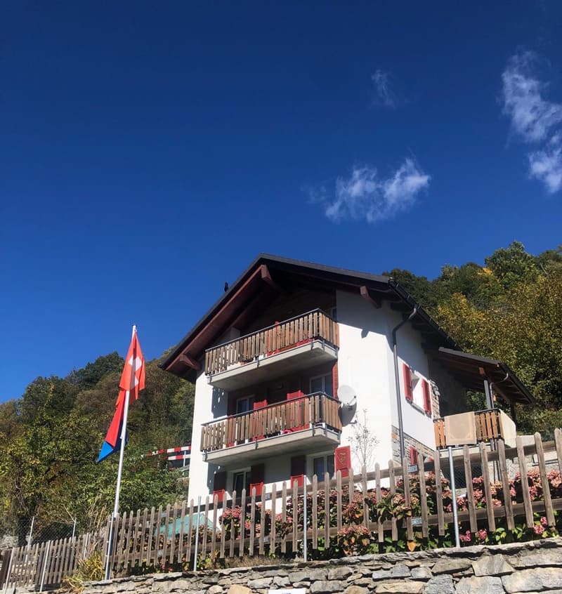 2 story house, white exterior, red shutters, wooden balconies, stone wall, flag