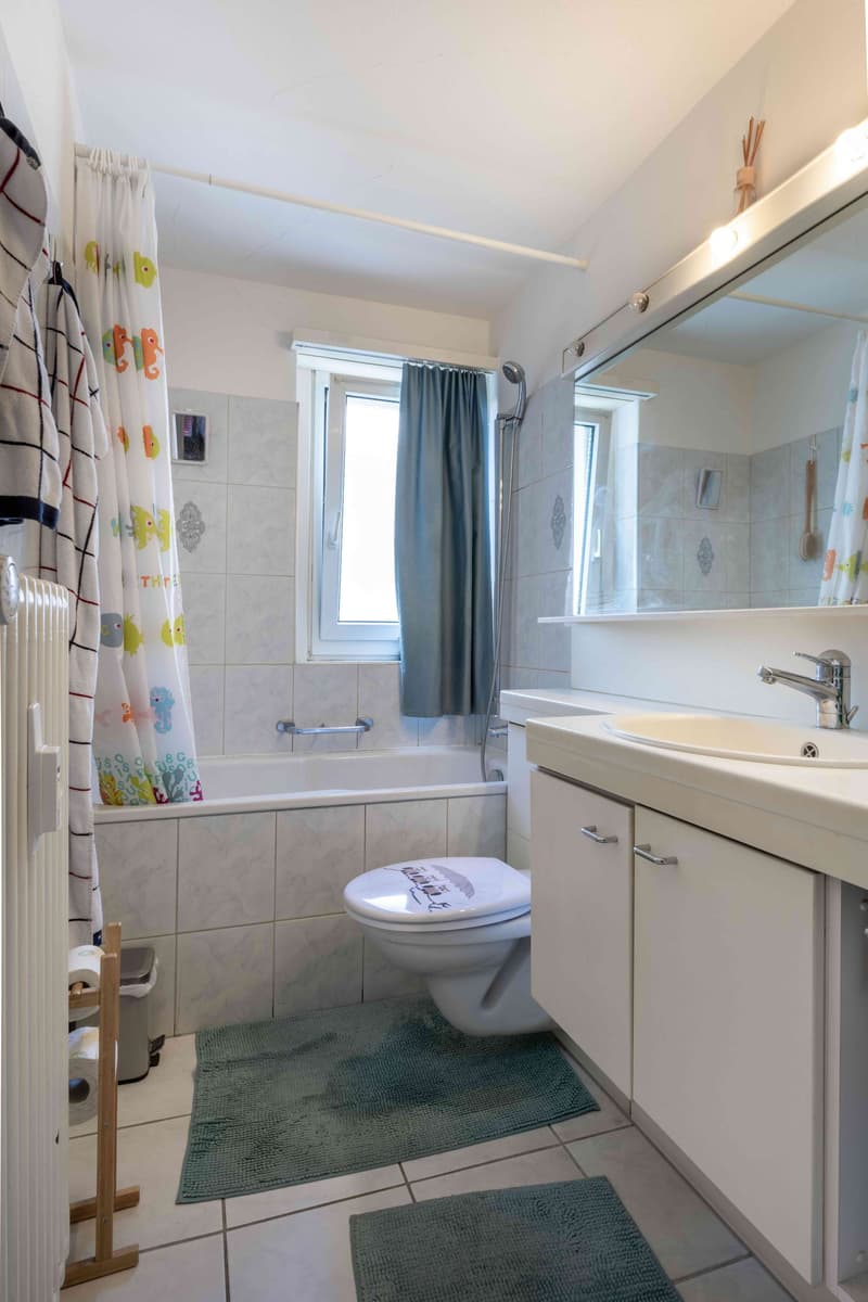 Bathroom with bathtub, toilet, sink, mirror, shower head, window, tiles, mats, radiator