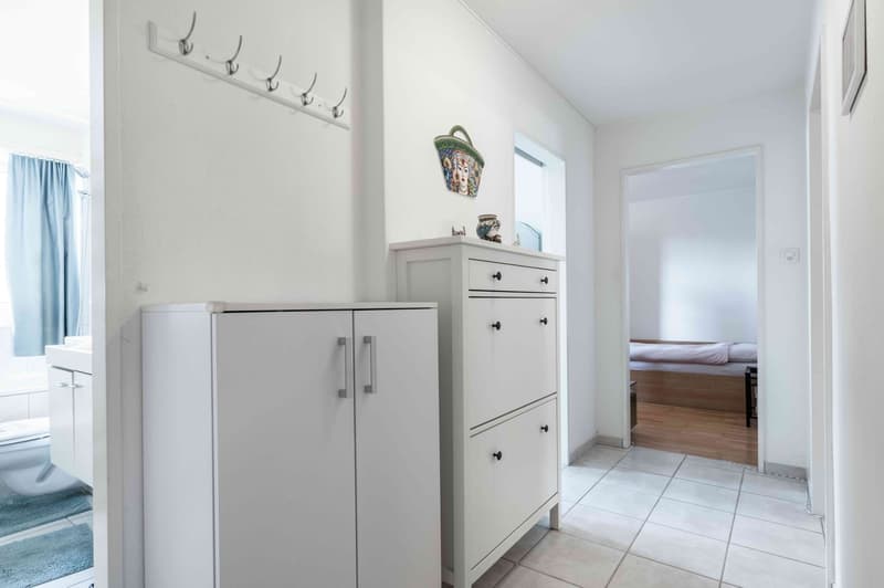 hallway with white cabinets, a coat rack, and a door leading to the bedroom and bathroom