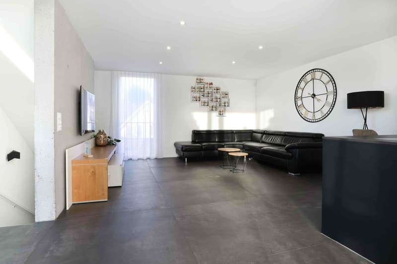 Contemporary living room with black leather sofa, wooden console table, flatscreen television, large clock, white curtains, wooden stools, wooden floor, black wall and white walls.