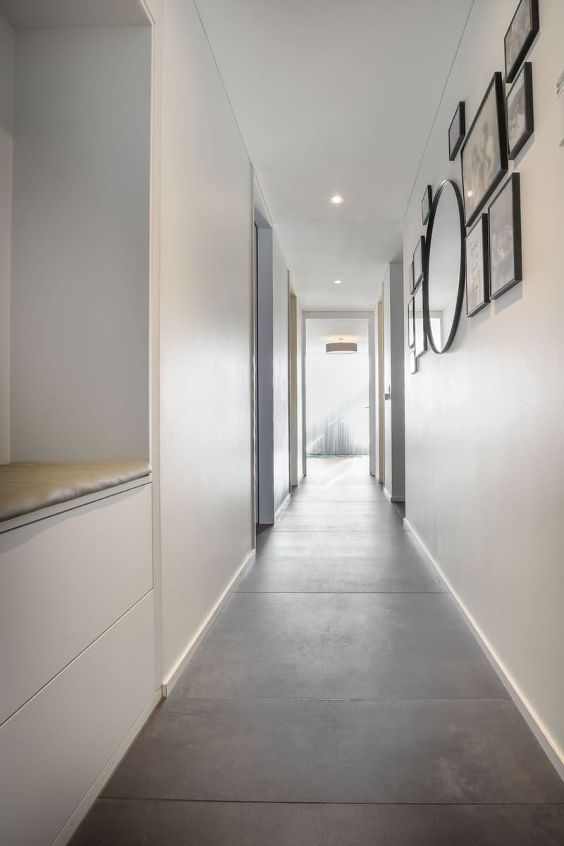 Gray floor, white walls, a built-in bench, a hanging mirror, photo frames on the wall, and a light fixture on the ceiling.