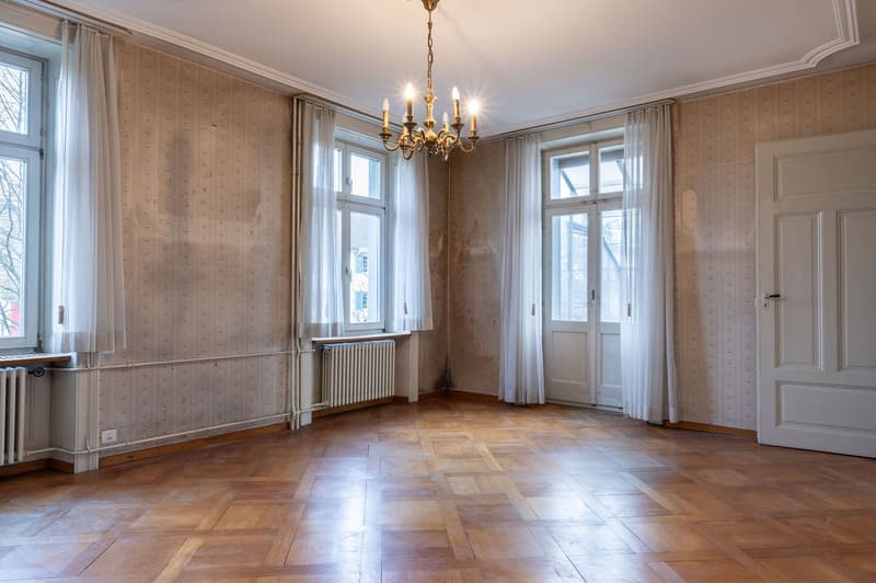 an empty room with wooden floor, white radiators, windows, and a chandelier