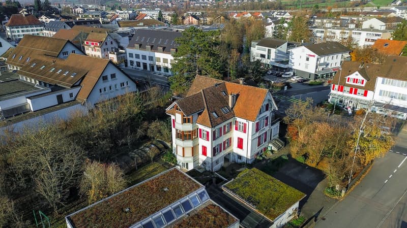 Two story house with brown roof, red windows, balcony, small garden