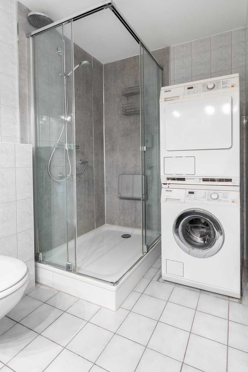 Modern bathroom with glass shower, white tiles, white toilet, Miele washing machine and dryer