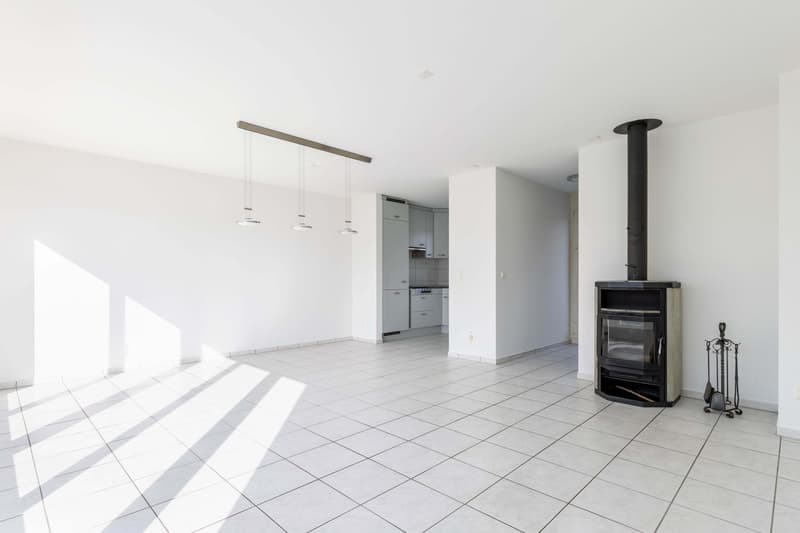 empty room, white tiles, white walls, fireplace, kitchen in the background