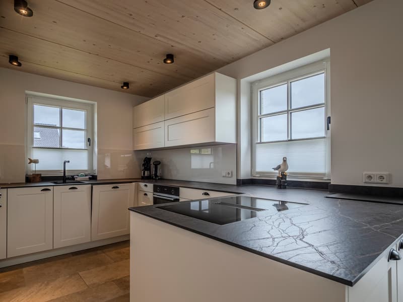 modern kitchen with white cabinets, black countertops, island with induction cooktop, windows, wooden floor