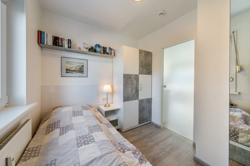 single bed, nightstand with lamp, white wardrobe, picture frame, shelves with books, radiator