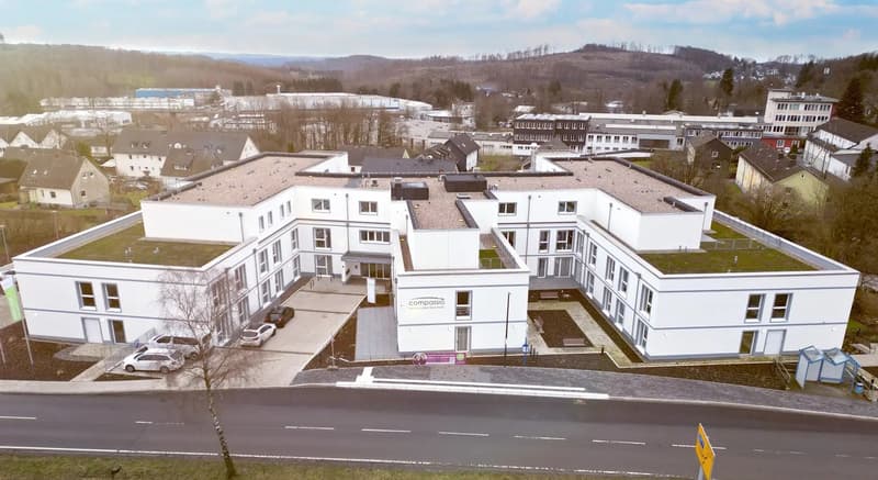 White building, multiple windows, parking lot, green roof, multiple cars parked