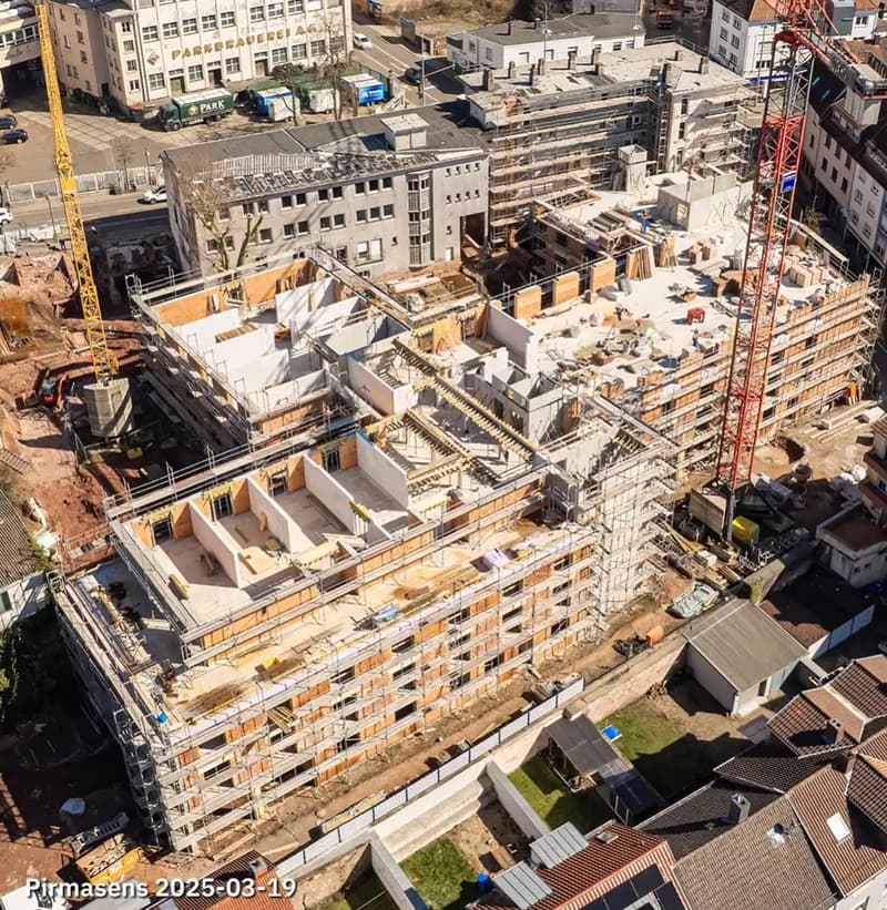 Aerial view of a multi-story building under construction with scaffolding, cranes, and construction vehicles visible.