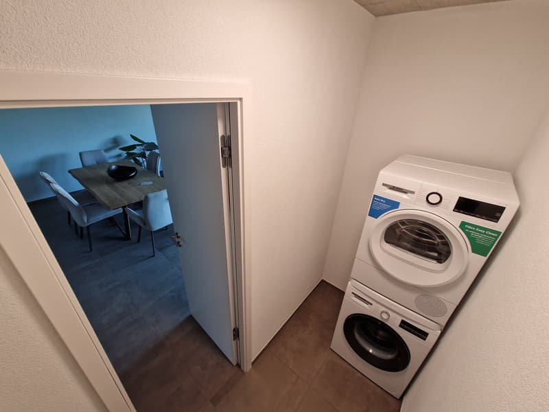 A small room with a washing machine and a door leading to a dining area