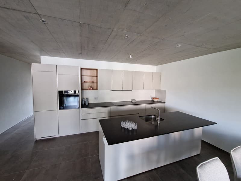 modern kitchen with white cabinets, black countertops, stainless steel island, built-in oven, sink with faucet, glasses on countertop