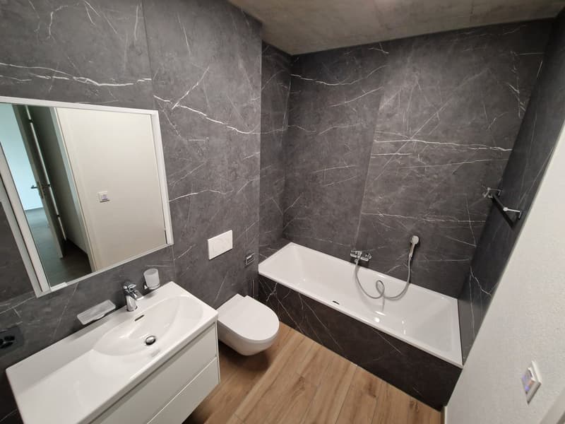 Bathroom with gray marble walls, white bathtub, white sink, white toilet, mirror, wooden floor