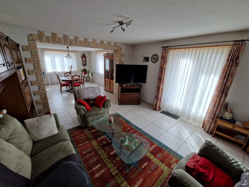 white tiled floor, large windows, white curtains, couch, armchair, coffee tables, TV, entertainment center, dining table, chairs, wooden cabinet, shelves, decorative items