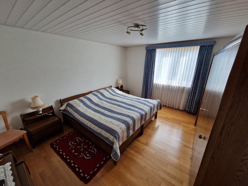 Bedroom with wooden floor, bed, nightstands, lamps, rug, window with curtains, wardrobe