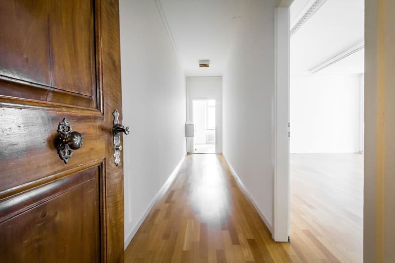 Empty hallway with wooden floor, white walls, and a door.