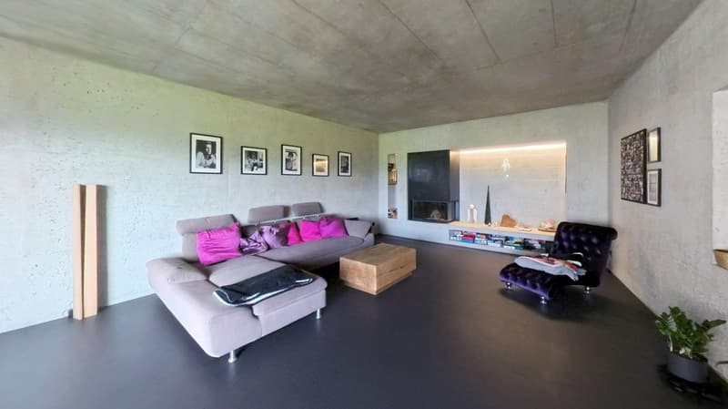 modern living room with concrete walls, gray sofa, wooden coffee table, fireplace, wooden floor, armchair, shelves, picture frames