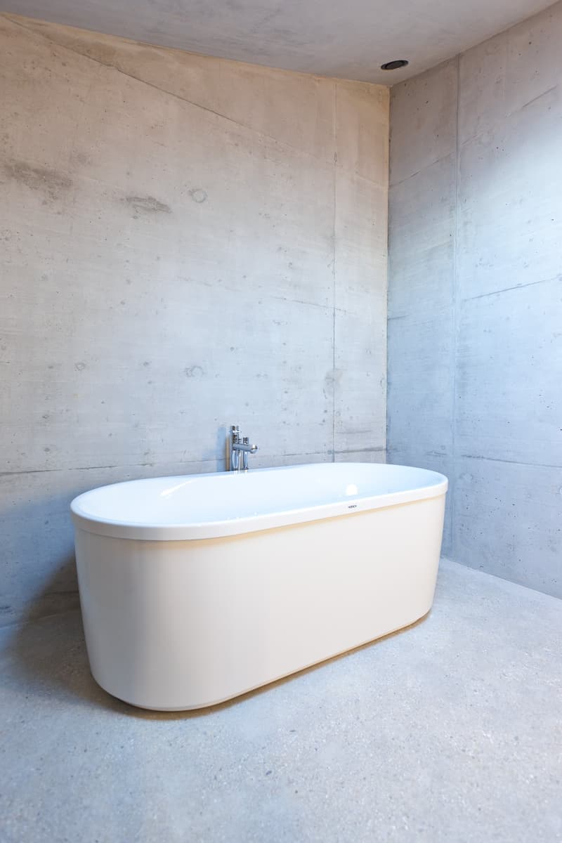 Bathroom with a white bathtub, concrete walls, and a silver faucet