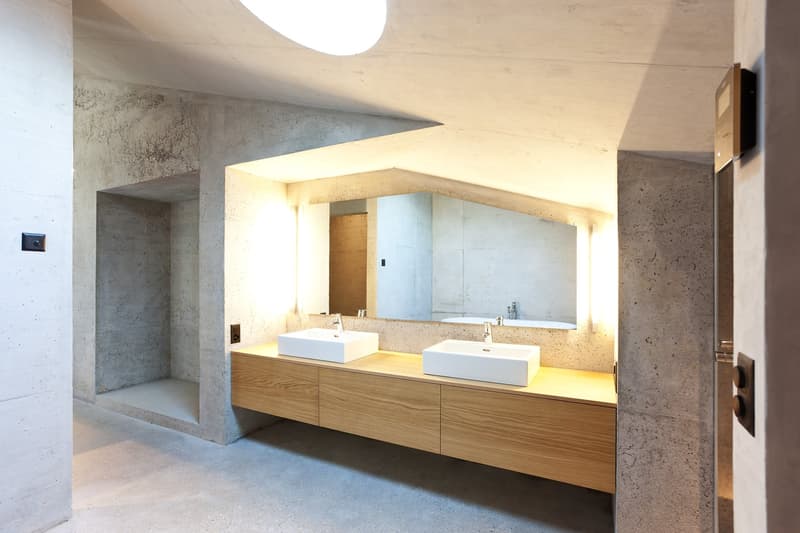 modern bathroom with concrete walls, wooden vanity, two sinks, large mirror, shower area