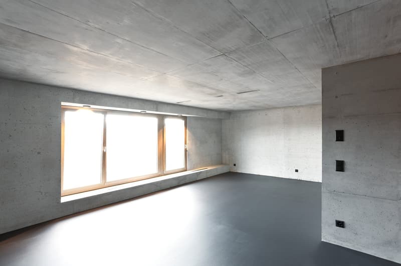 Empty room with concrete walls, large window, gray floor