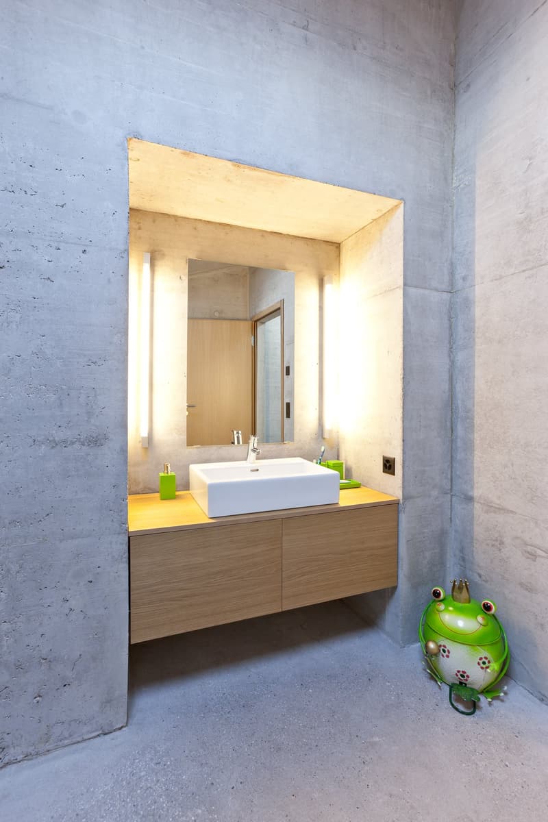 Bathroom with concrete walls, wooden cabinet, white sink, mirror, and decorative frog
