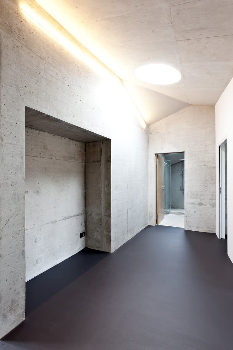 Empty room with concrete walls, black floor, and a glass door leading to a shower room
