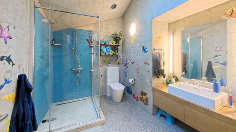 Bathroom with blue tiles, glass shower enclosure, white toilet, wooden vanity with sink, wall-mounted towel rack, decorative wall stickers with sea creatures, mirror, and a towel hanging on a hook.