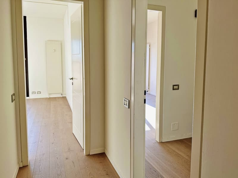 Empty hallway with wooden floors, white walls, and open doors leading to other rooms.