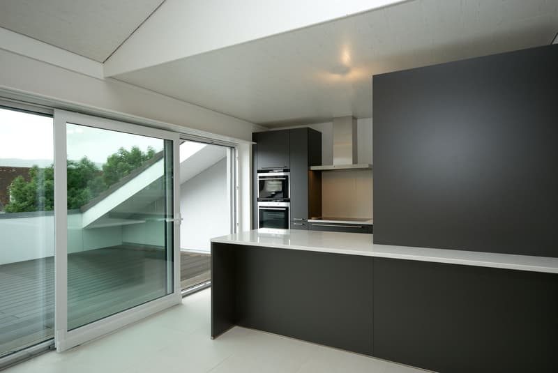 modern kitchen with white tiles, black cabinets, white countertop, large glass doors leading to balcony