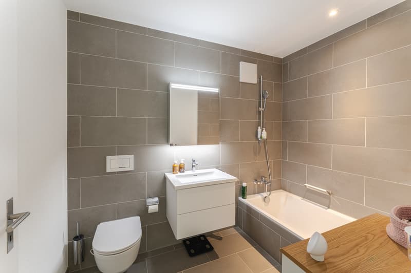 modern bathroom with white tiles, white sink, white toilet, bathtub, shower, wooden countertop