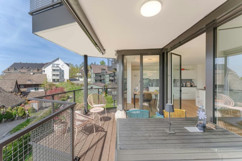 balcony with wooden floor, metal railing, glass doors, table, chairs, lamp, plants, view of the town