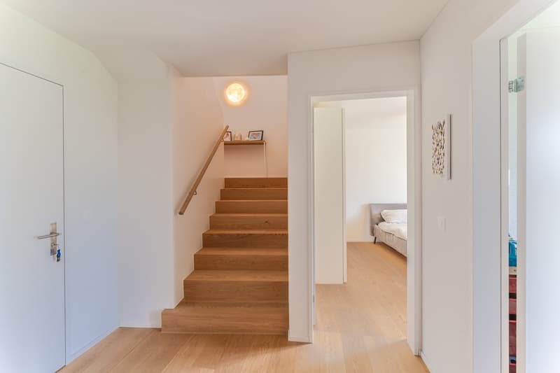 wooden stairs, white walls, wooden floor, white door, small shelf with picture frames, light on the wall