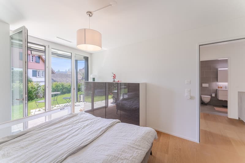 modern bedroom with large windows, sliding doors to balcony, wooden floor, white walls, bed, cabinet, lamp, toilet, sink