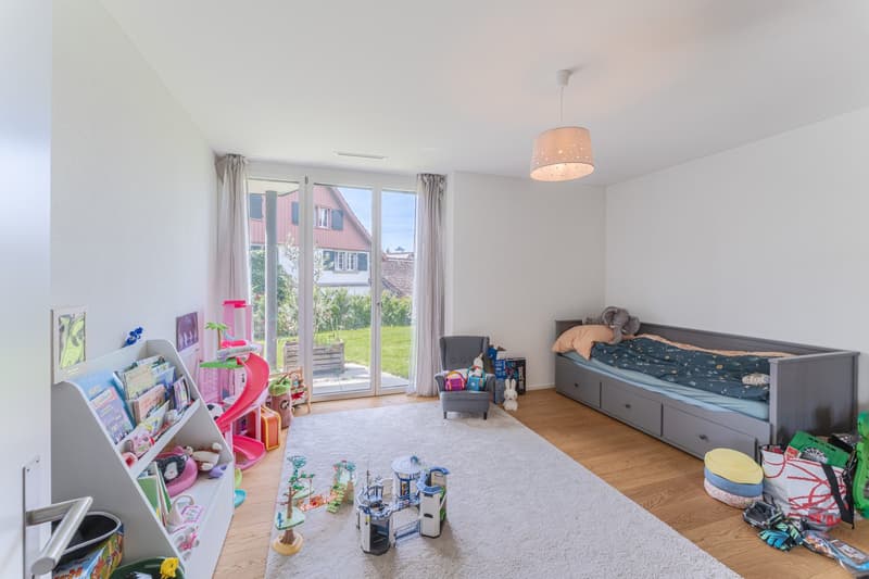 Children's room with a bed, toys, a chair, a shelf, a rug, and a glass door leading to a garden