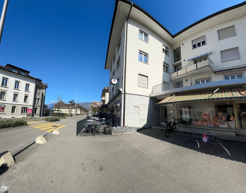 A 4 story apartment building with a balcony on the second floor, surrounded by road with parked bicycles and parked cars