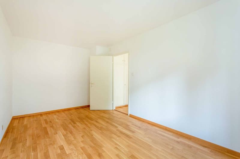 Empty room with white walls and wooden floor, open doors leading to another room