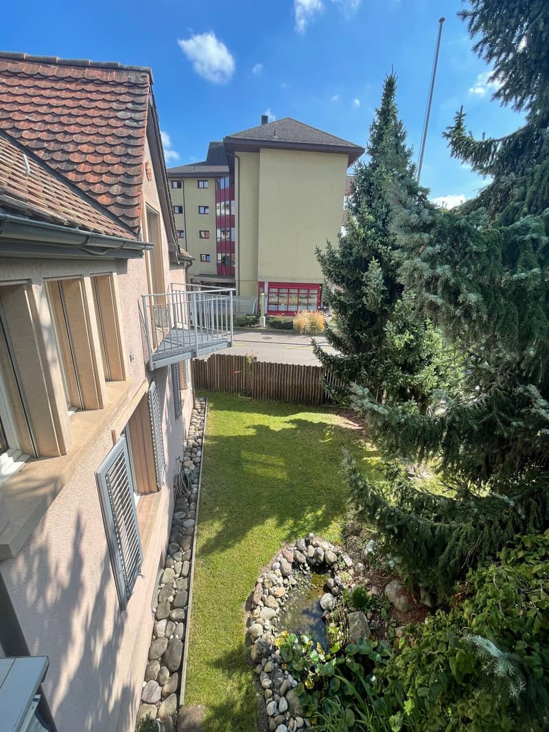 Terrace with wooden railing, garden with grass and stone pathways, multi-story building with red tiles
