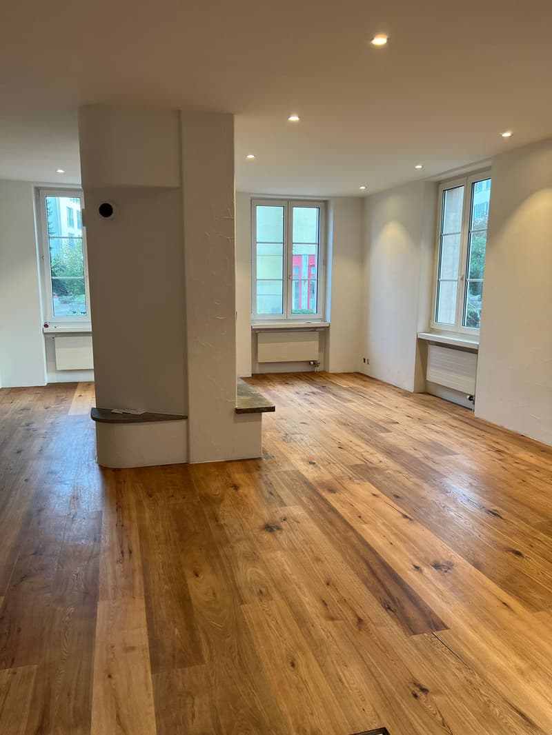 empty room with hardwood floors, three large windows, central column, recessed lighting