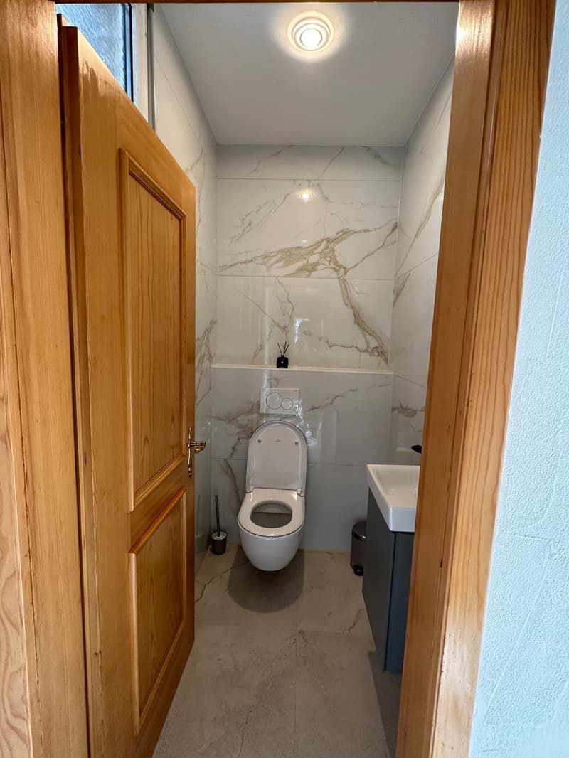 Bathroom with wooden door, toilet, sink, and modern tile flooring