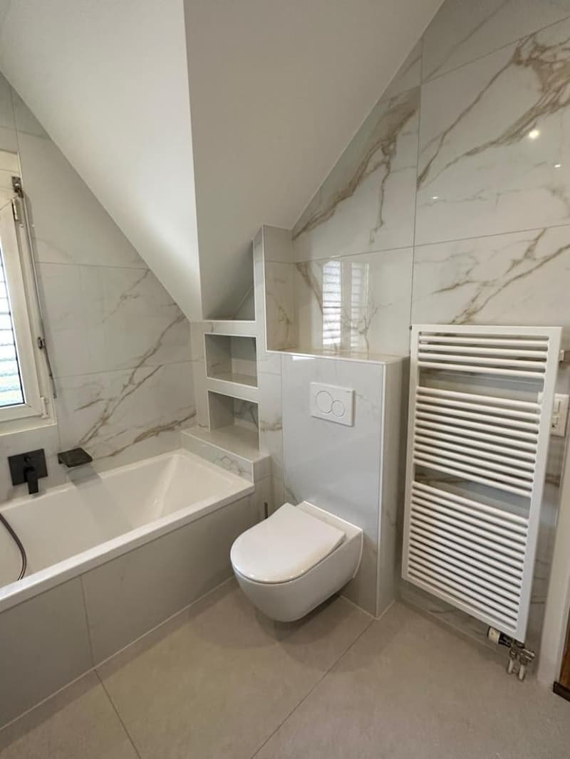 modern bathroom with white marble tiles, corner bathtub, built-in shelves, wall-mounted toilet, and white radiator