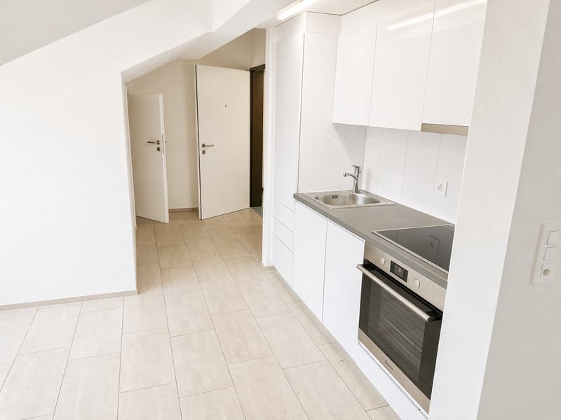 Empty kitchen with white cabinets, tiled floor, sink, oven, and a door leading to another room