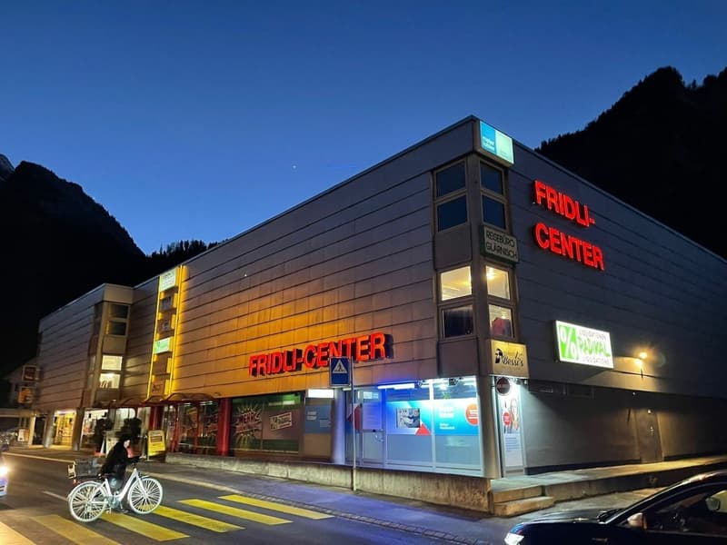 A large building with a sign that reads 'FRIDLI-CENTER', multiple windows, and a person riding a bicycle in front.