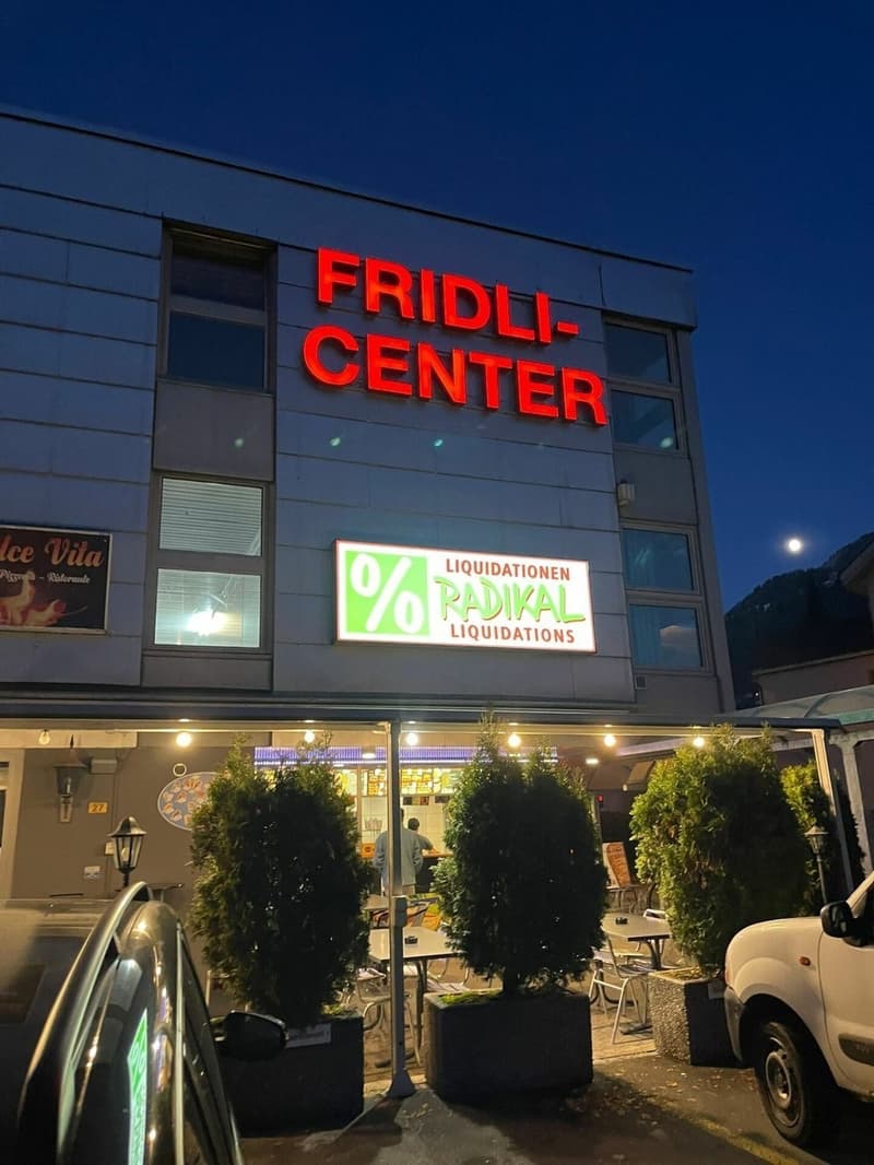 Fridli-Center building with a signboard, outdoor seating area, and parked cars