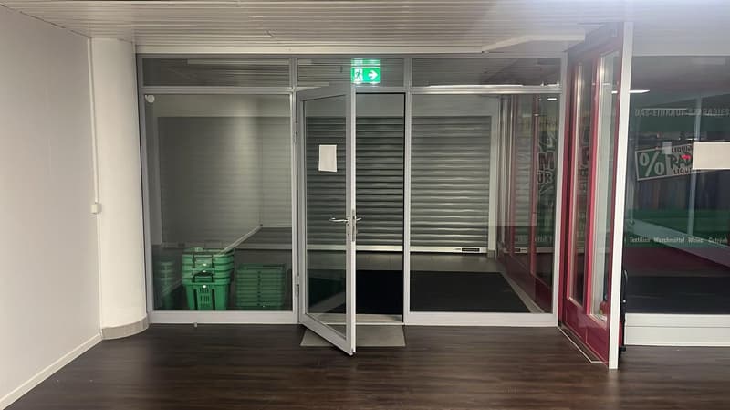 Open entrance with glass doors, wooden floor, green storage boxes, exit sign