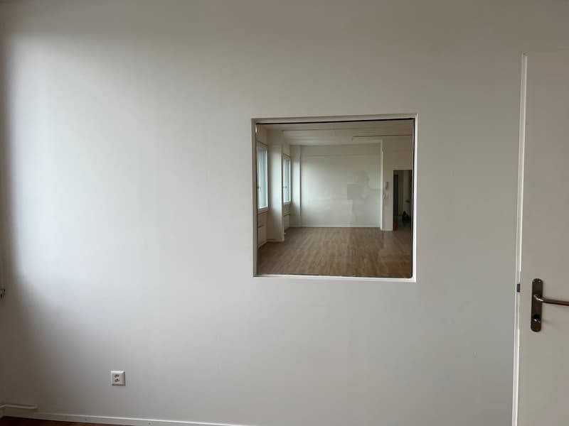 white walls, wooden floor, small square window, power outlet, door
