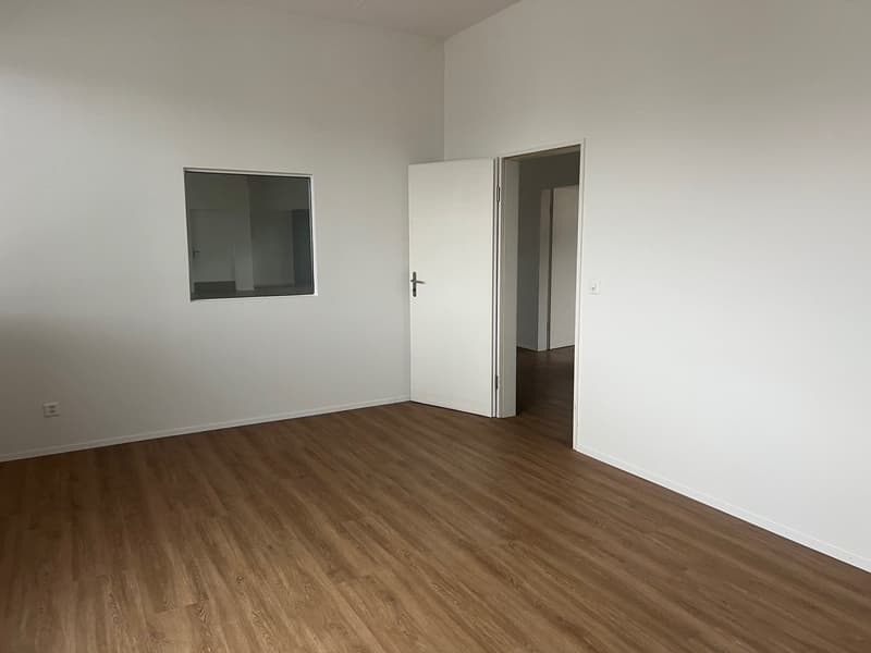 Empty room with white walls, wooden floor, and doors.