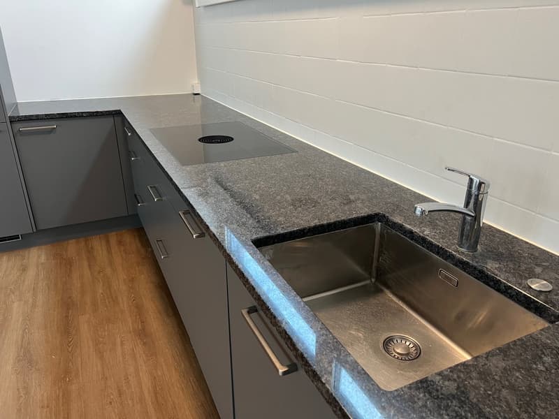 Granite countertop, silver sink, induction cooktop, stainless steel faucet, wooden floor, gray cabinets