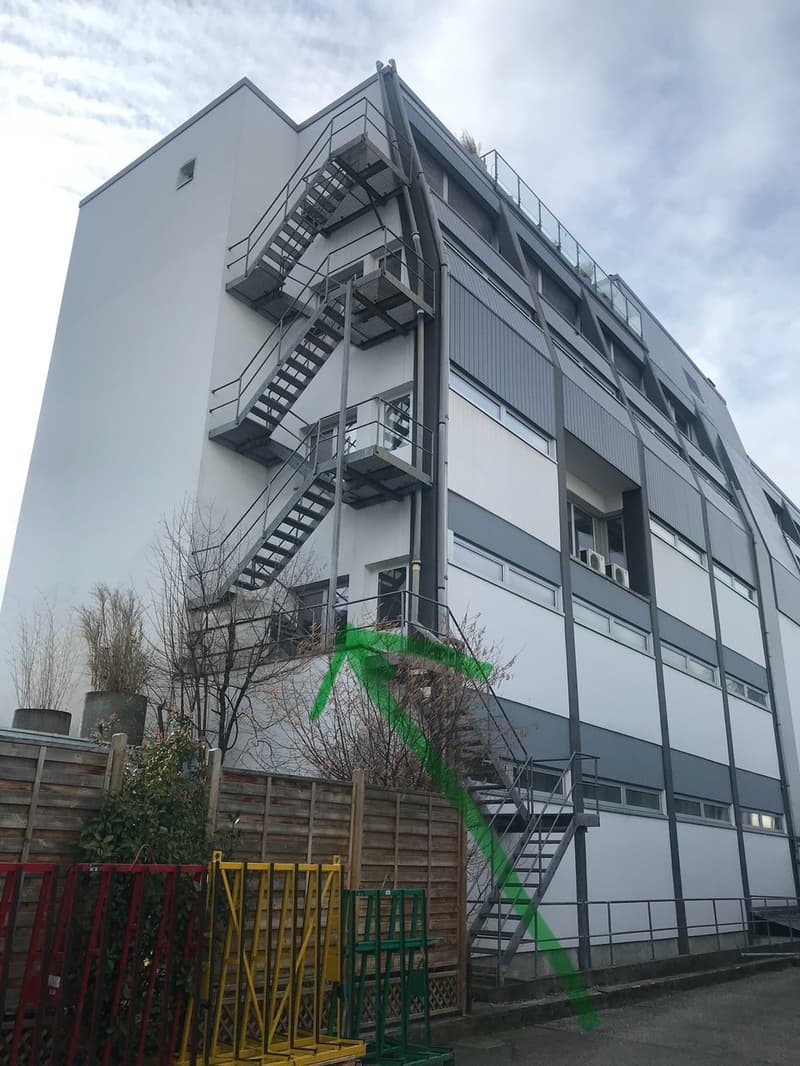 A large modern building with grey walls, white windows, three storeys and emergency stairs