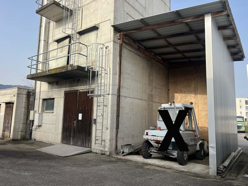 Industrial building with a garage entrance, a forklift parked inside, metal railings, and a metal roof.