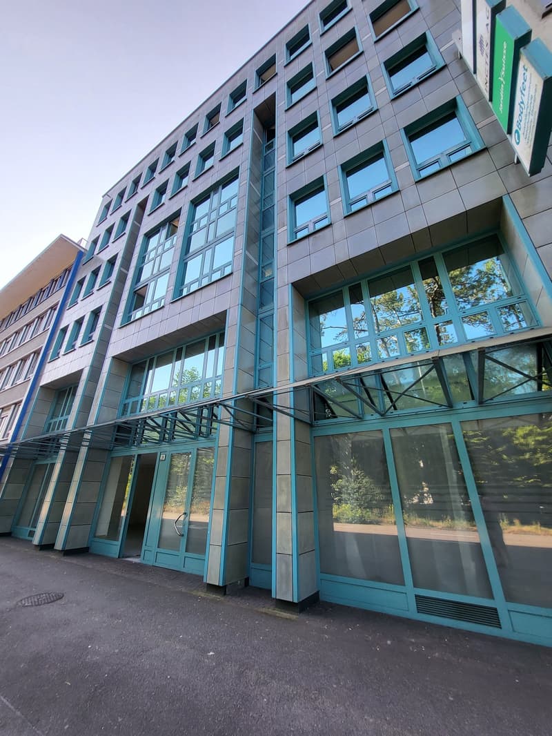 Multi-story commercial building with glass facade, large windows, and a parking area in front.